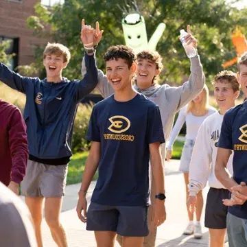 student on walking into campus on first day of class, arms up cheering 